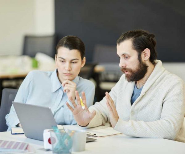 Brand Managers Coworking Two young brand managers sitting together at office desk discussing some problems looking at laptop screen